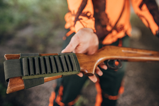 Young man in hunting gear standing in forest with rifle