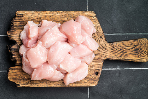 Diced raw chicken meat, uncooked poultry fillets. Black background. Top view.