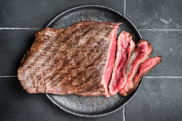 istock Grilled Flap or Flank Steak, sliced on a plate. Black background. Top view 1464127142