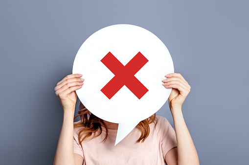 No concept. Girl holding poster with a red prohibition cross sign isolated on a gray background