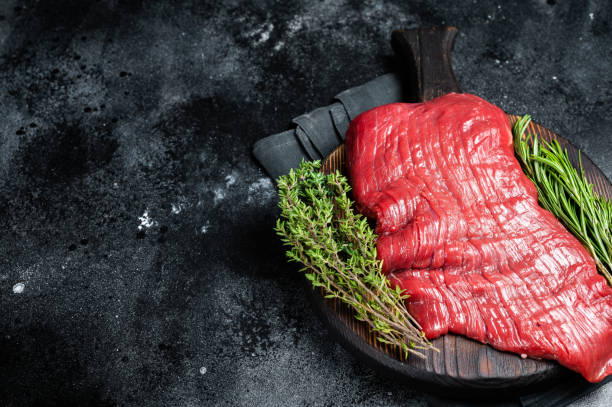 istock Raw flank beef steak, uncooked meat with herbs. Black background. Top view. Copy space 1464127528