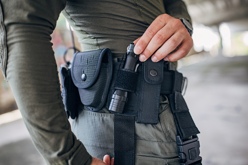 Close-up of a young man standing in tactical gear with belt on his hip taking flashlight
