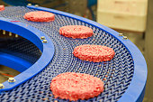 Closeup view of pure beef burgers on factory conveyor chain.