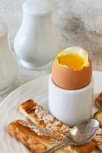 Stock photo showing close-up view of white plate containing eggcup with boiled dippy egg and buttered, white toast soldiers for breakfast.