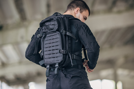 Young man putting military backpack on a back getting ready for work