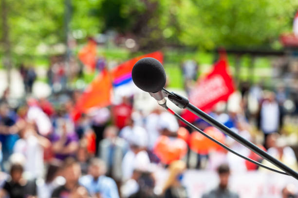 istock Protest, public demonstration or pension reform strike, focus on microphone, blurred crowd of people in the background 1464141473