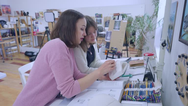 Woman artist shows a girl on a model of a part of a human head how to draw the contours of a face correctly.