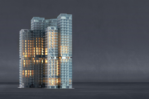 Front view of a 3D architectural model of a modern high rise office building made of steel and glass, with many windows illuminated, on a neutral concrete background with copy space on the side. Conceptual background for real estate, construction industry, building information modeling (BIM) and facility management.