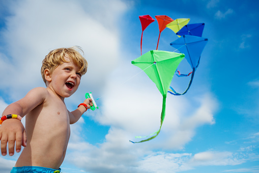 Close-up of a little boy smile, laugh stand holding many kites in hand and looking at them smiling over blue sky