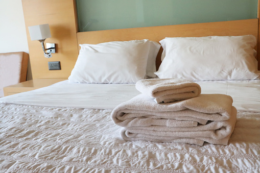 Stock photo showing close-up view of pile of folded, white towels sitting on hotel room duvet bedding.