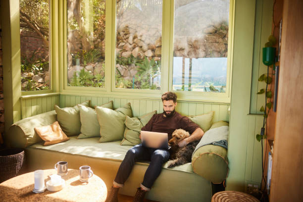 istock Young man using a laptop on a sofa with his dog 1464150112