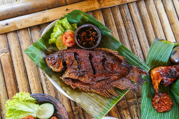 Grilled gurami or grilled gurame with red barbecue sauce, vegetables and chili sauce served on banana leaves