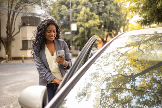 giovane donna che tiene il telefono mentre apre la porta di uber - taxi travel business women foto e immagini stock