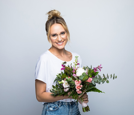 Portrait of happy beautiful woman holding flower bouquet against gray background