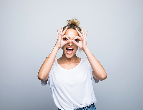 Happy woman making eyeglasses with hands against gray background