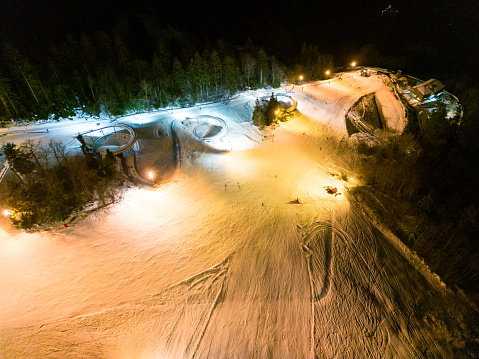 Night ski slope with lights, aerial view of a small skiing resort in winter.