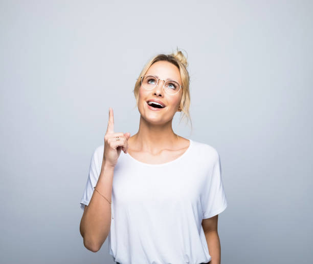 smiling thoughtful woman pointing and looking up - pointing women cheerful front view imagens e fotografias de stock