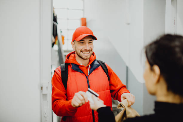 istock Smiling delivery man taking a credit card from a customer while delivering an order 1464159731