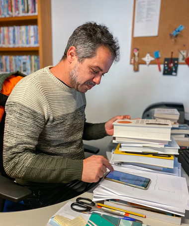 Male librarian at his desk surrounded by books using mobile phone