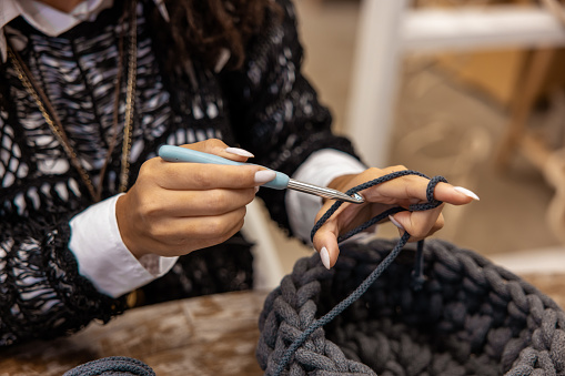 Cropped photo of a craftswoman on the table grabbing a strand of yarn with a metal crochet hook