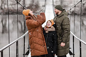 Young mother, father and the little daughter catches snowflakes in a beautiful winter park during a snowfall. It is snowing. family is playing in the snow. Winter activities. the winter holidays.