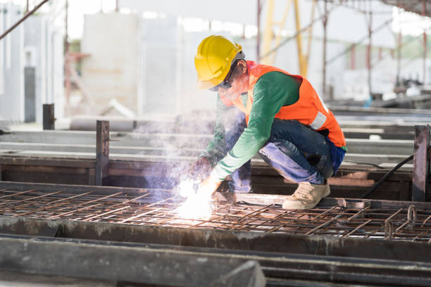 Industrial scene showing a welder using a torch to perform precise metalwork in a dimly lit environment.
