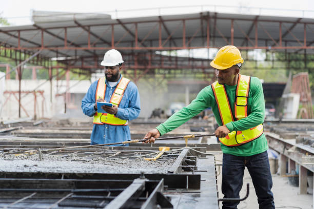istock Construction worker uses long steel trowel spreading wet concrete pouring at precast concrete wall construction site. Worker or mason working or making smooth surface of concrete with equipment tool 1464165212