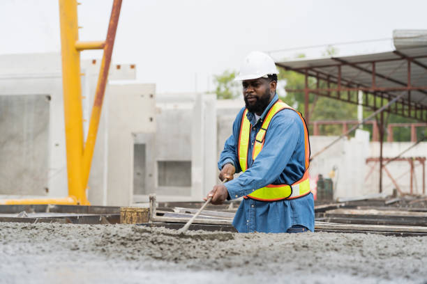 istock Construction worker uses long steel trowel spreading wet concrete pouring at precast concrete wall construction site. Worker or mason working or making smooth surface of concrete with equipment tool 1464165213