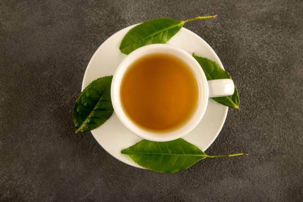 feuilles de thé avec une tasse de thé vert, sur fond noir - chinese tea photos et images de collection