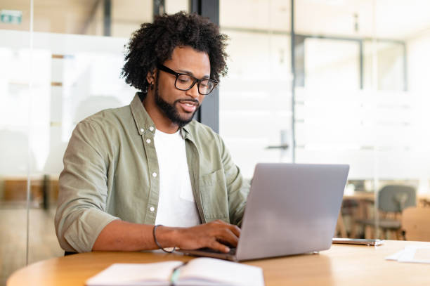 istock Focused curly handsome man using laptop computer in contemporary coworking space 1464167216