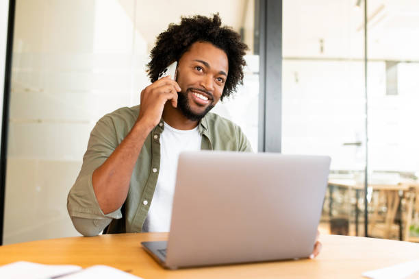 istock Confident young entrepreneur using laptop and talking on mobile phone in contemporary co-working space 1464167242