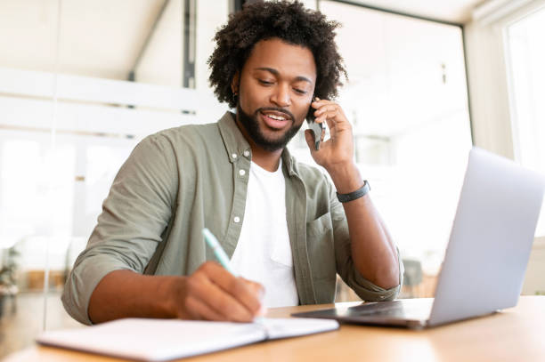 istock Confident African-American businessman talks phone writing down some notes sitting in the office 1464167335