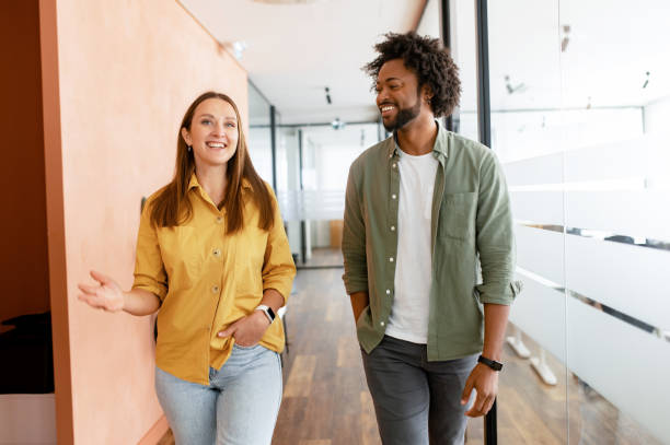 Couple of business people discussing tasks walking in the office hall Couple of business people discussing tasks walking in the office hall. Two diverse colleagues have small talk during break. Friendly atmosphere in team two adults stock pictures, royalty-free photos & images