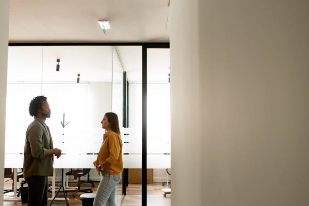 istock Two colleagues discussing something during coffee break, coworkers have friendly conversation standing in modern hallway with the glass wall on the background 1464167683