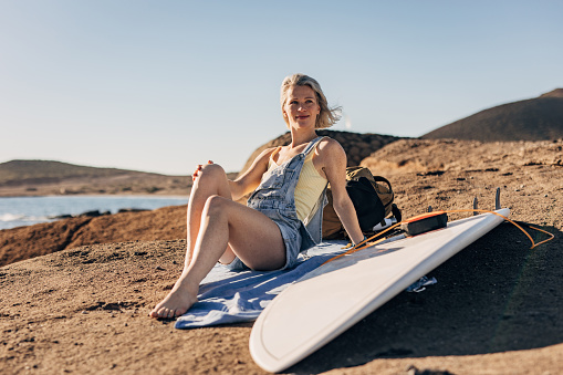 One woman, beautiful female surfer sitting on the beach by the sea.