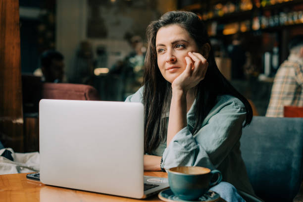 istock A young brunette work remotely on a laptop sitting in a coffee shop. 1464168610