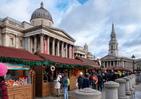 People shopping at the annual Christmas market in Trafalgar Square, London, with the National Gallery and St Martin-in-the-Fields church behind.