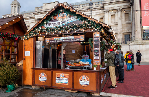 Hungry customers at a German sausage stall in Trafalgar Square, London, with the National Gallery behind. The sausage stall is part of the annual pop-up Christmas Market held on the upper part of the Square.