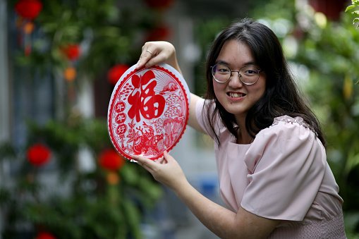 An Asian teenage girl is feeling cheerful while holding with 'Fu' translates prosperity poster.