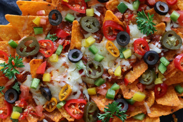 istock Full frame image of homemade, loaded nachos covered in melted mozzarella cheese, cherry tomatoes, black olives, Jalapeno peppers, grey muslin, black background, elevated view 1464174145