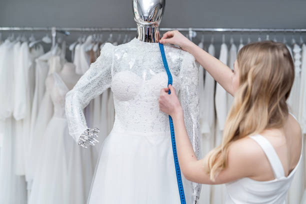 A pretty sales consultant measures a wedding dress for a client and shows impeccable quality. A pretty sales consultant measures a wedding dress for a client and shows impeccable quality. Bridal store wedding dress designer stock pictures, royalty-free photos & images