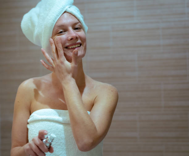 istock Young woman smiling while massaging her face in home bath, copy space, skin care routine 1464185349