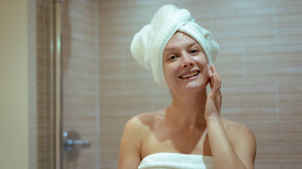 istock Young woman smiling while massaging her face in home bath, copy space, skin care routine 1464185369
