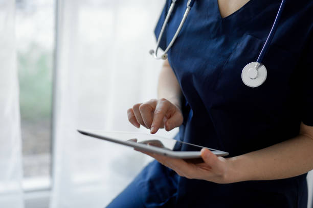 istock Doctor woman using tablet computer while standing near panorama window in clinic, close up. Physician or surgeon at work. Medicine concept 1464186349
