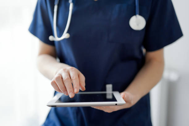 istock Doctor woman using tablet computer while standing near panorama window in clinic, close up. Physician or surgeon at work. Medicine concept 1464186381