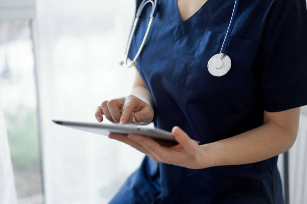 istock Doctor woman using tablet computer while standing near panorama window in clinic, close up. Physician or surgeon at work. Medicine concept 1464186391
