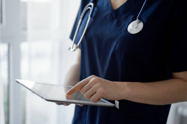 istock Doctor woman using tablet computer while standing near panorama window in clinic, close up. Physician or surgeon at work. Medicine concept 1464186548