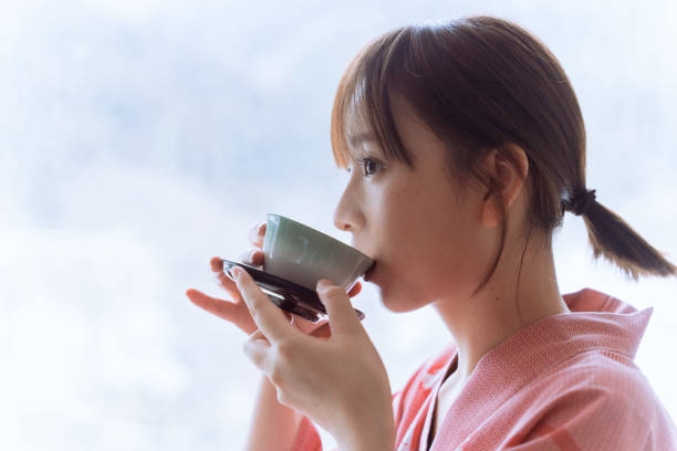 冬の間、雪の中の山の自然の景色を望む部屋でくつろぎながら熱いお茶を飲む着物を着たアジアの若い女性 - tea women cup drinking ストックフォトと画像