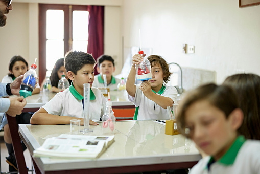 Waist-up view of teacher watching as schoolboys create a working lung model and better understanding how humans breathe.