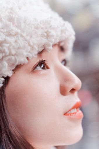 Close up side shot of the face of a young smiling Asian adult woman, wearing warm winter clothing, looking at the views and landscape, feeling amazed and relaxed, while enjoying the atmosphere.

Young happy Asian female traveler or tourist having fun and relaxing on a solo-trip or travel in Japan during winter holidays, enjoying her day outdoors.
